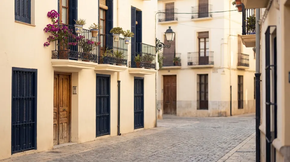 Calle de casas bajas con balcones de forja, macetas y contraventanas azules